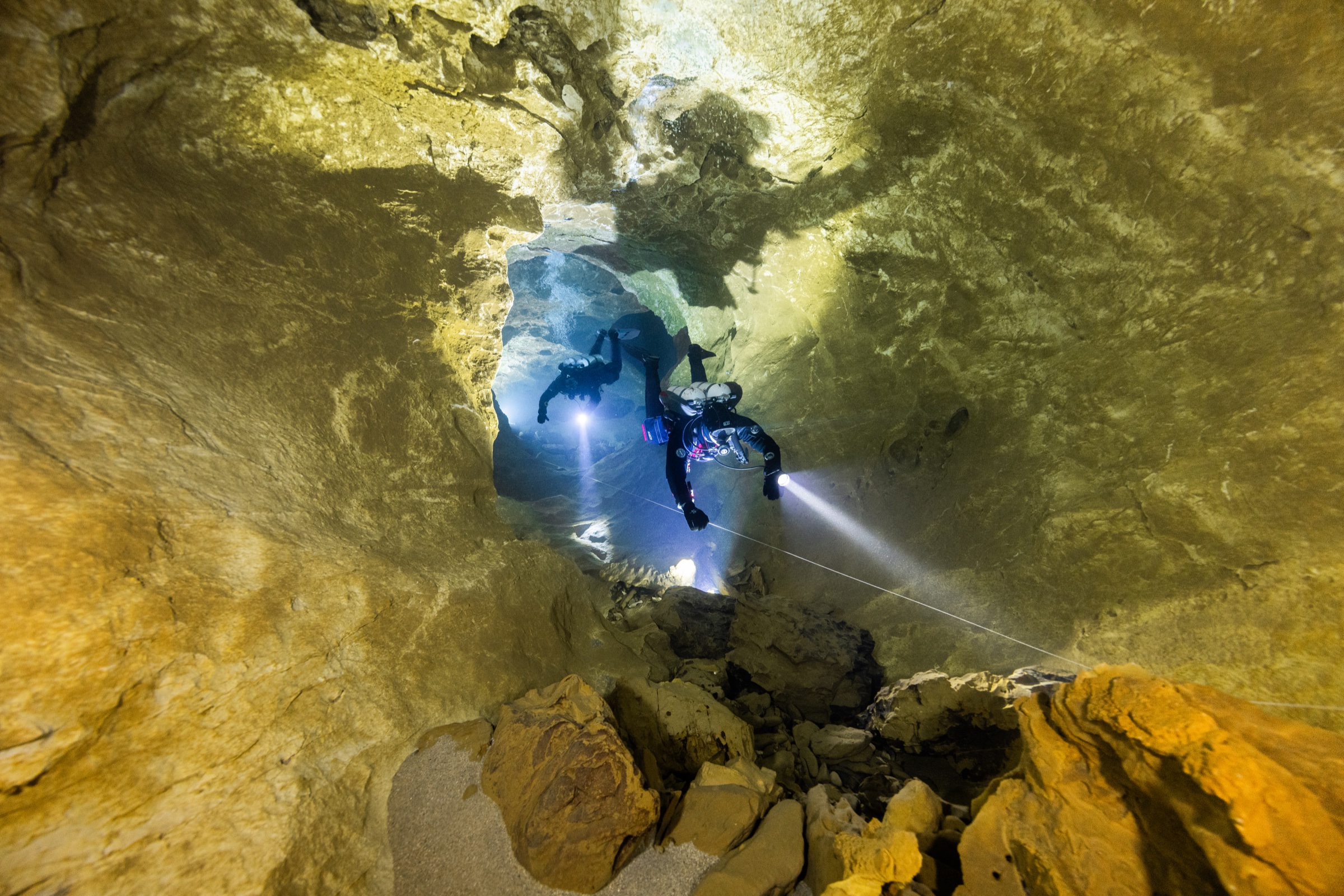 Two divers with torch beams in a cave passage