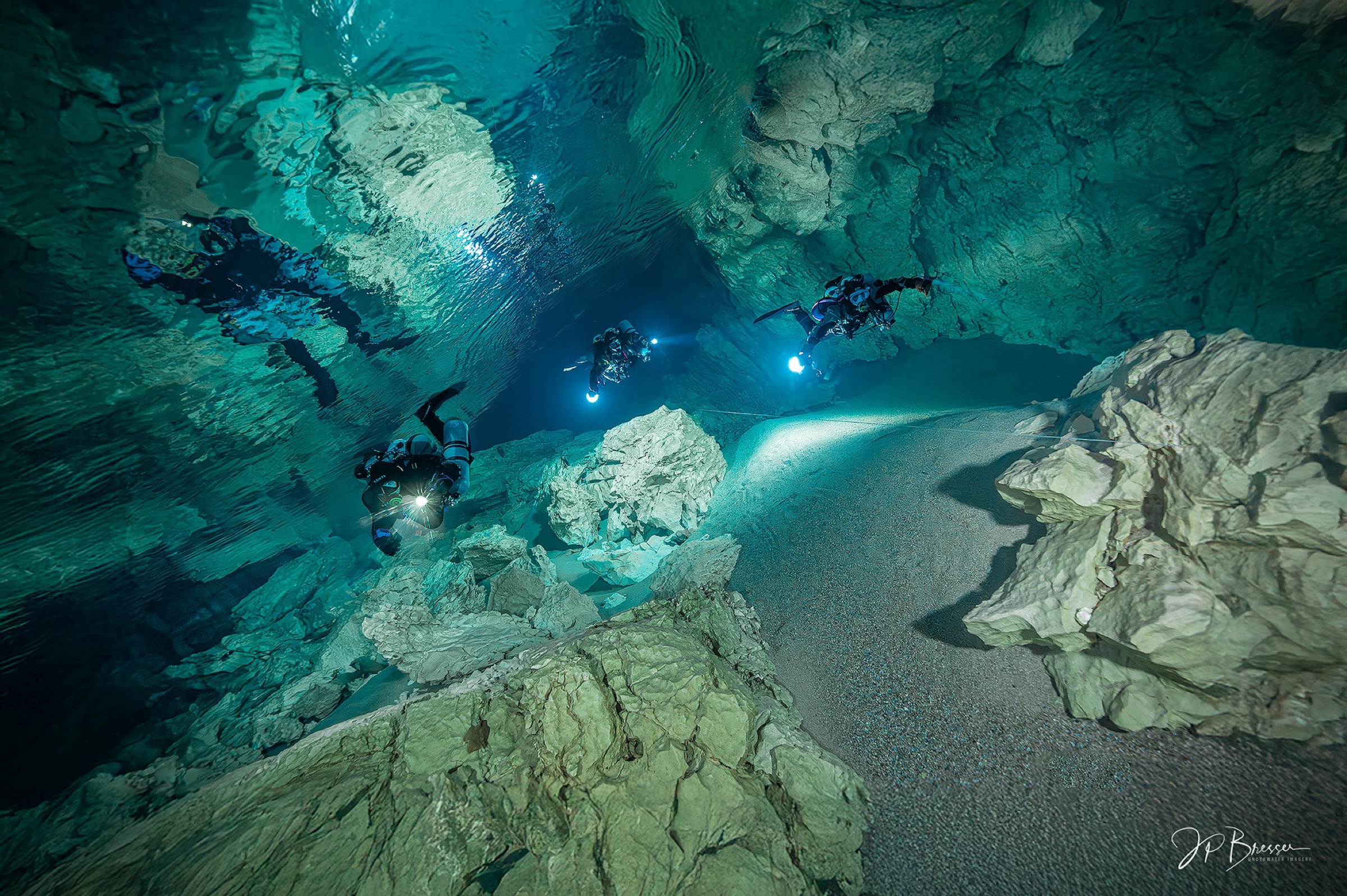 Three divers exploring a cave with sand floor