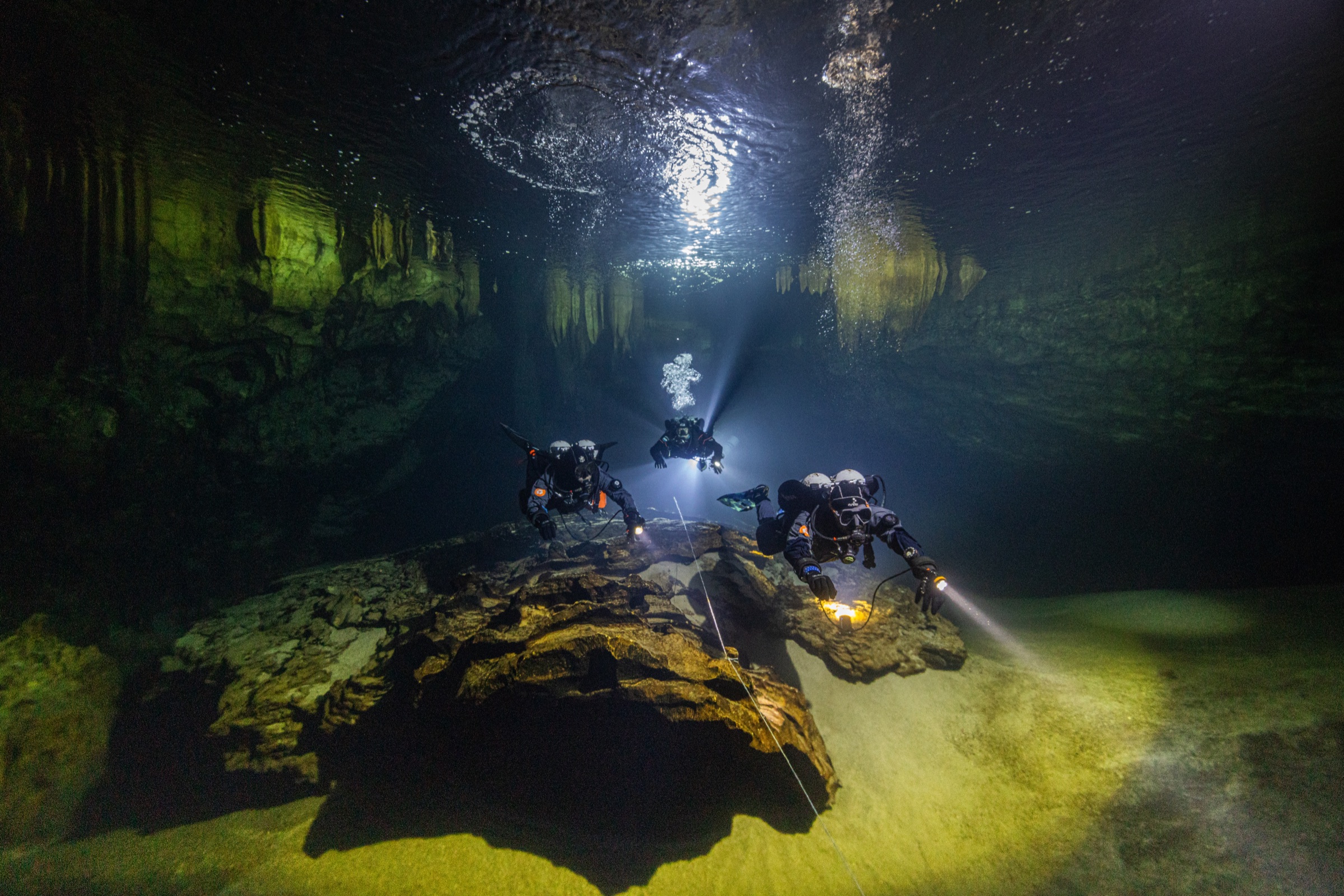 Three divers training in cave with stalactites
