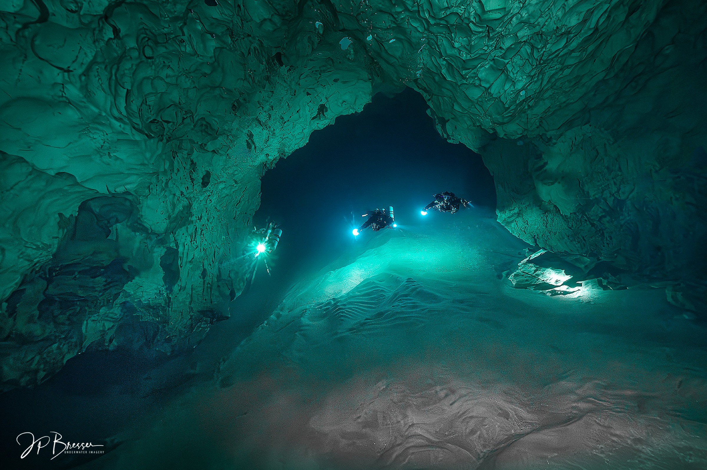 Two divers in a wide teal cave passage