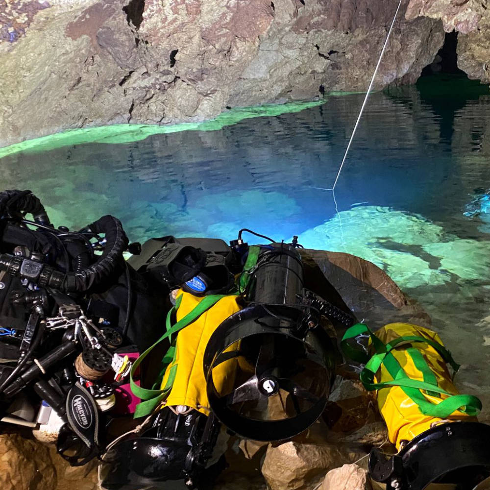Survey gear and DPVs staged at a cave water edge